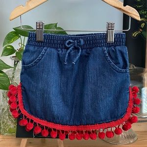 Denim skort with red pom pom trim curved hem